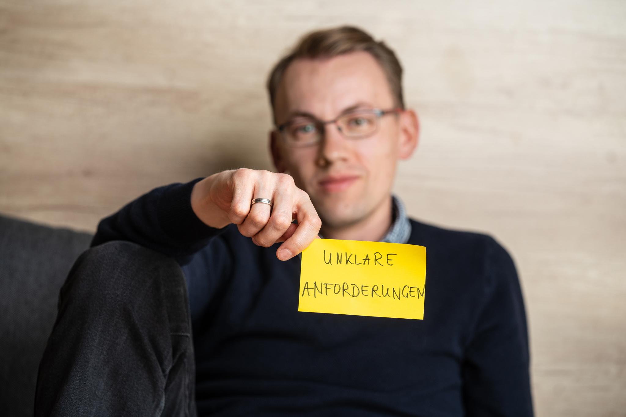 Person hält Post-it mit der Aufschrift "Unklare Anforderungen"
