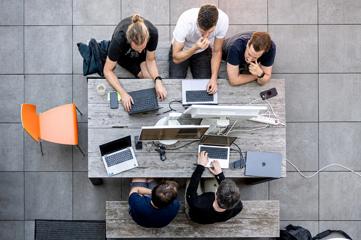 Blick von oben auf ein DevBoost Engineering Team, das gemeinsam mit Kunden an mehreren Laptops an der technischen Umsetzung arbeitet.